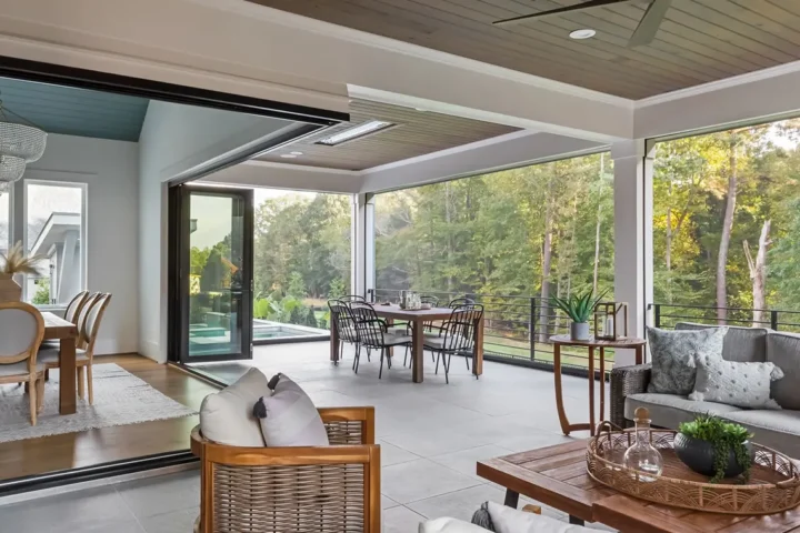 Spacious modern screened-in porch with large sliding glass doors, outdoor dining area, comfortable seating, and forest view.