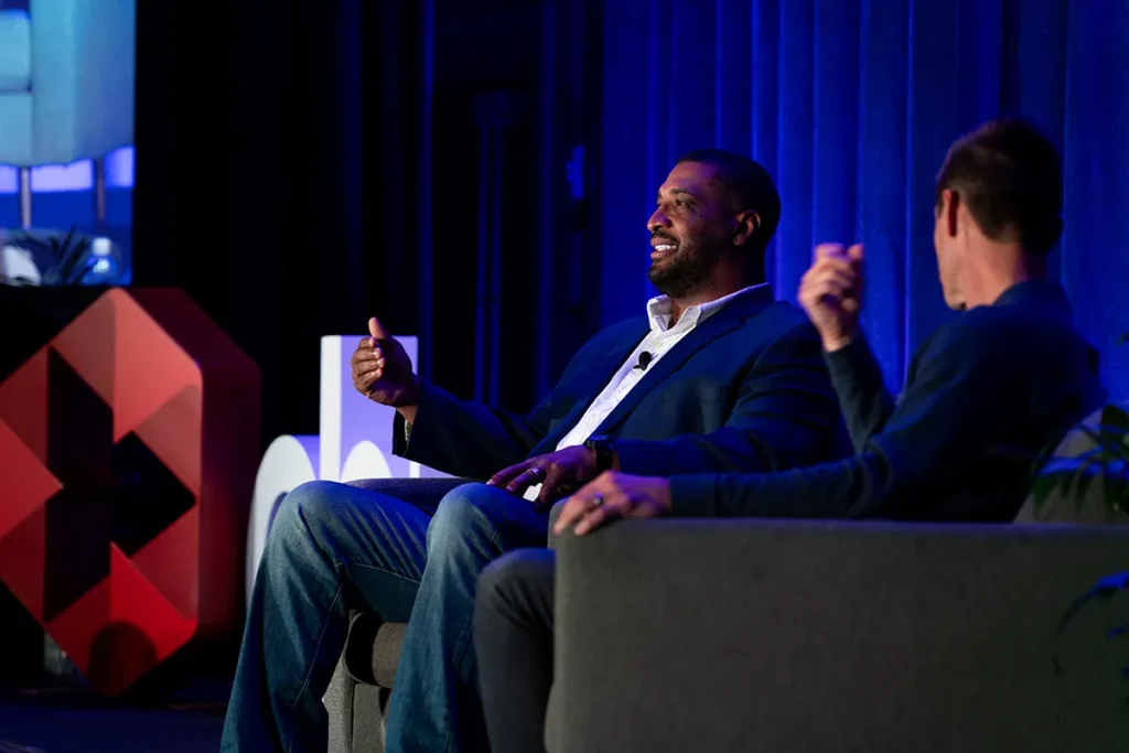 Two men sitting on chairs on stage, speaking