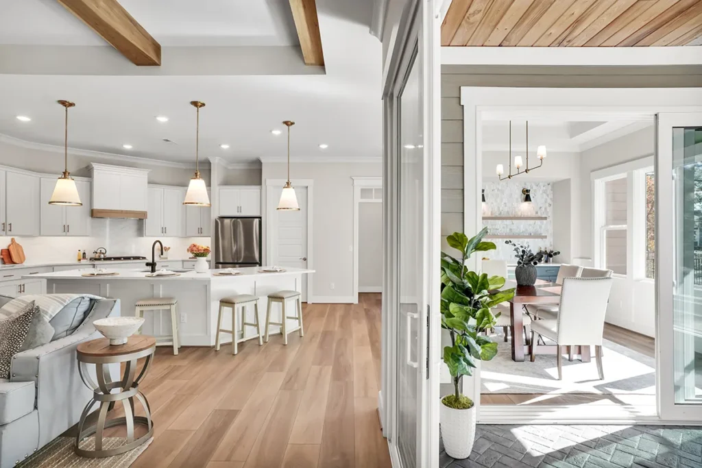 Bright open-concept kitchen with white cabinets, wood beam ceiling, pendant lighting, and island seating leading into a dining area