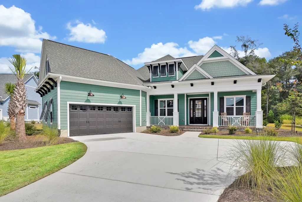 Green craftsman-style house exterior with covered porch, two-car garage, and landscaped front yard under blue sky