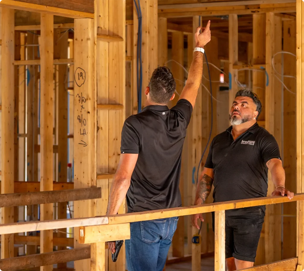 Two construction professionals reviewing framing progress inside a home under construction.