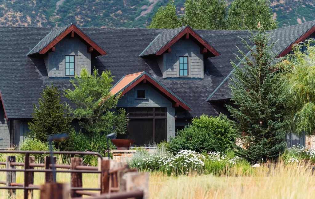 Gray home with gabled dormers and wood trim surrounded by trees and landscaped gardens