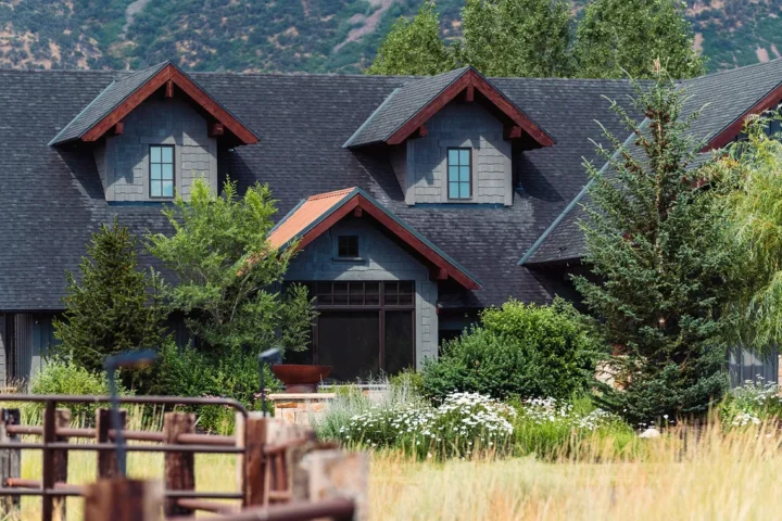 Gray home with gabled dormers and wood trim surrounded by trees and landscaped gardens